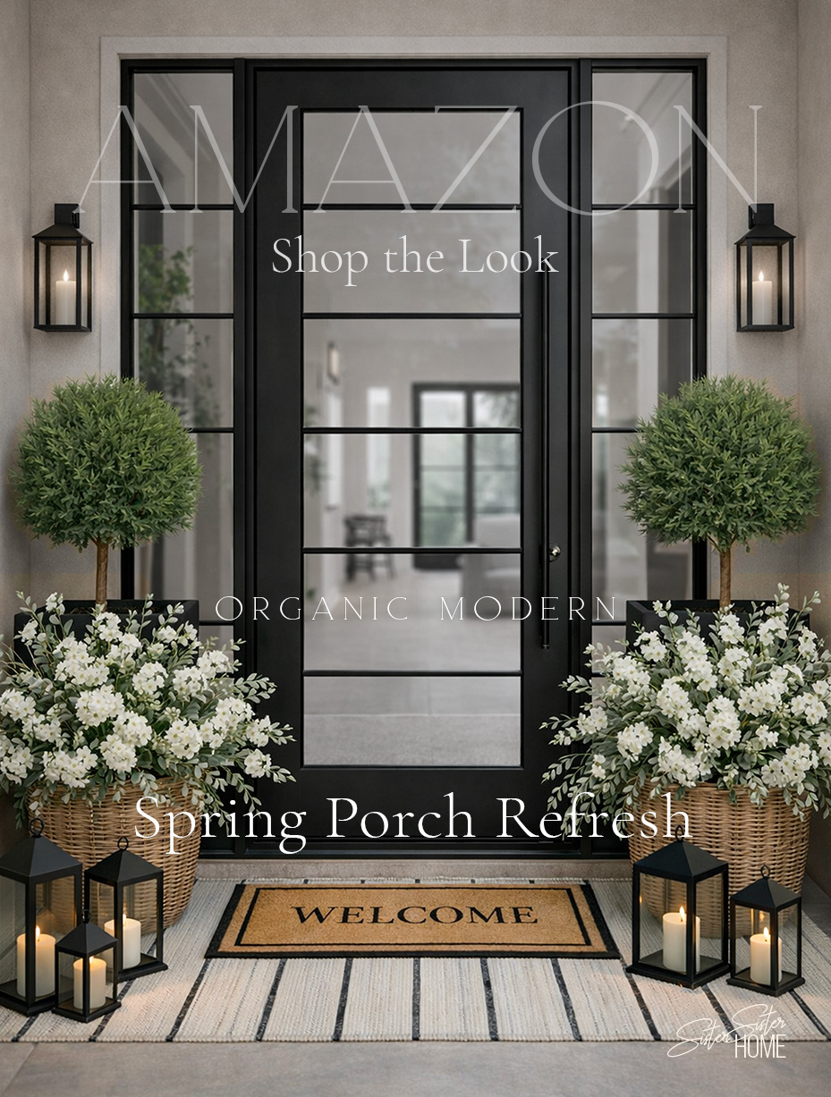 Organic modern spring porch with black front door, topiary trees, white flowers, lanterns, and striped outdoor rug