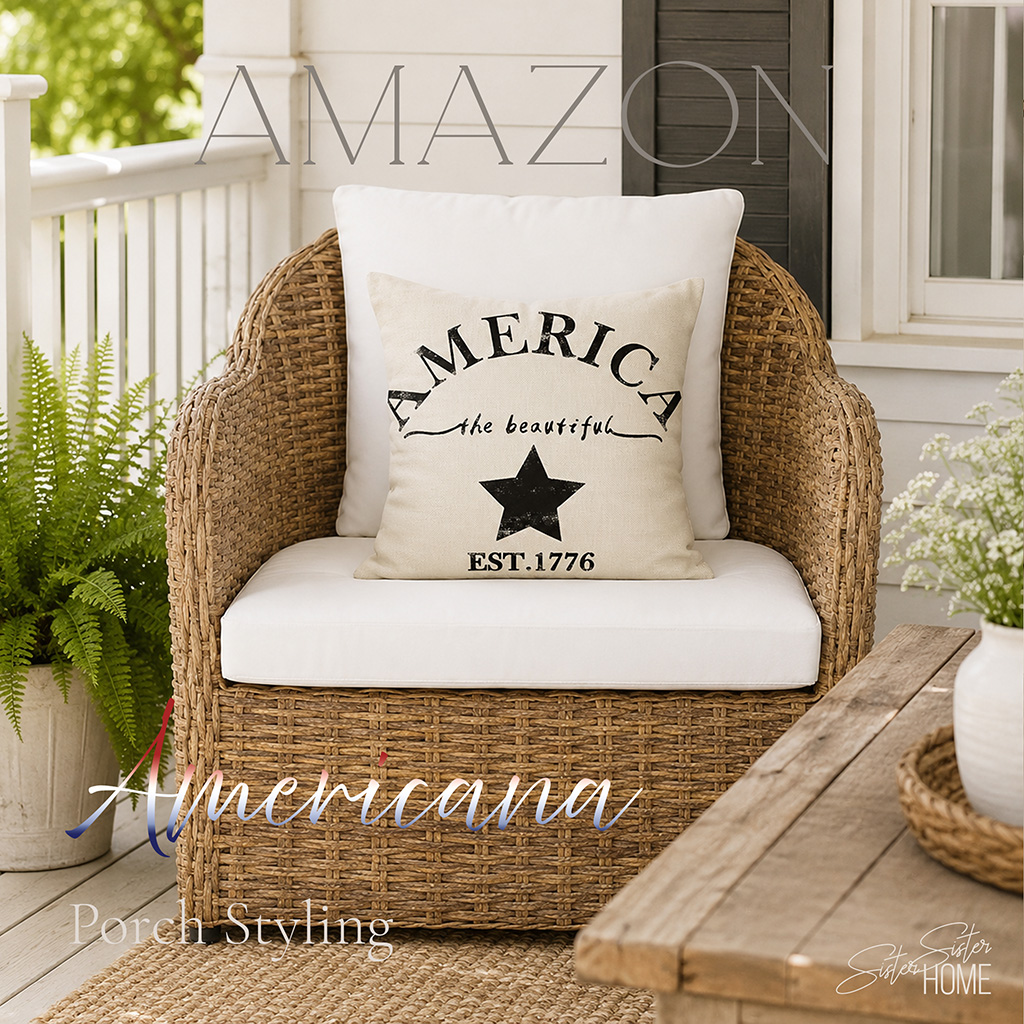 Americana porch styling with a natural rattan outdoor chair, white cushions, patriotic pillow, rustic wood table, greenery, and neutral summer porch decor.
