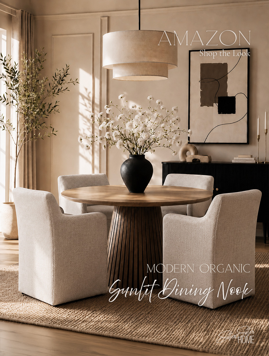 Sunlit modern organic dining nook with a round fluted wood table, upholstered chairs, black sideboard, abstract art, and warm neutral styling.